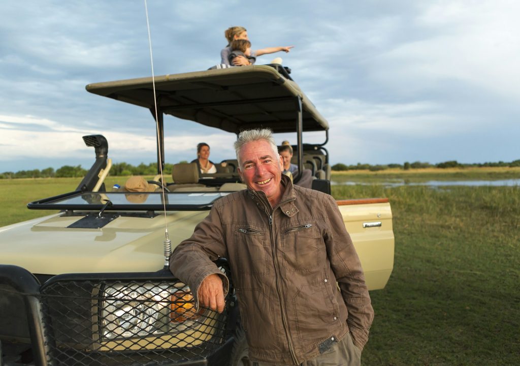 A smiling safari guide and family of tourists in a safari vehicle.